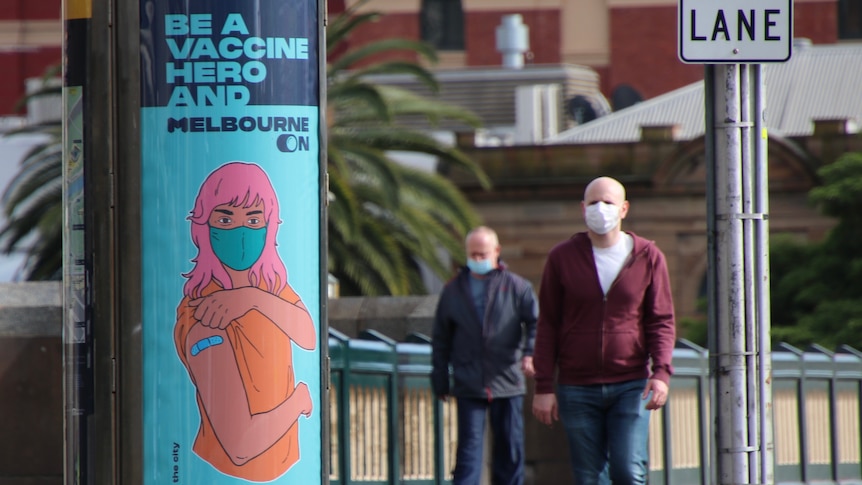 Two men walk across a Melbourne CBD bridge with a COVID vaccination poster in view