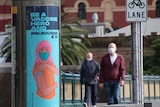 Two men walk across a Melbourne CBD bridge with a COVID vaccination poster in view