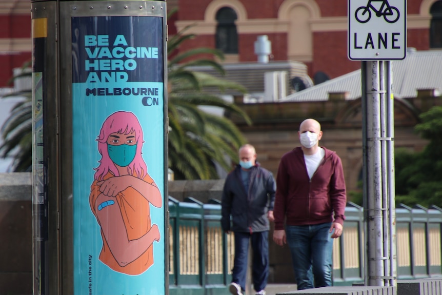 Two men walk across a Melbourne CBD bridge with a COVID vaccination poster in view