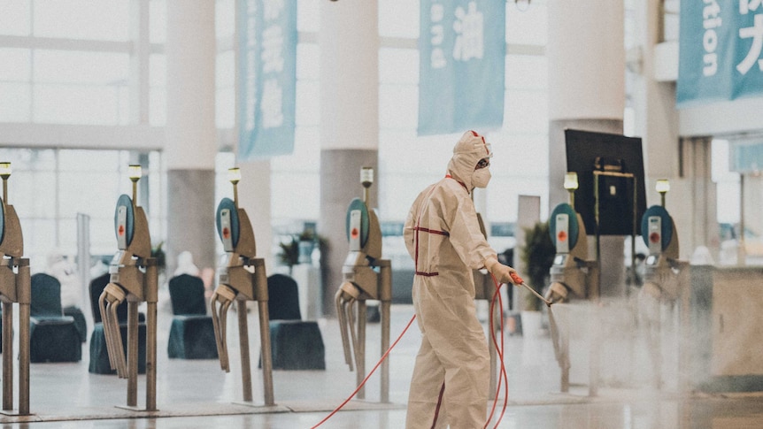 A person in a hazmat suit sprays disinfectant in a building in China