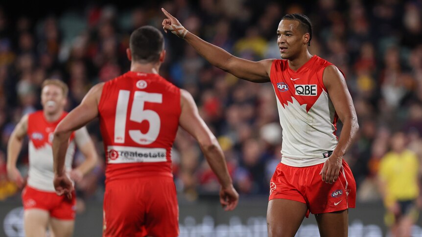 A Sydney Swans forward points in the air, as he walks back after a goal.
