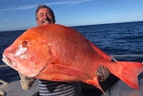 man holding large red coloured fish with ocean in the background