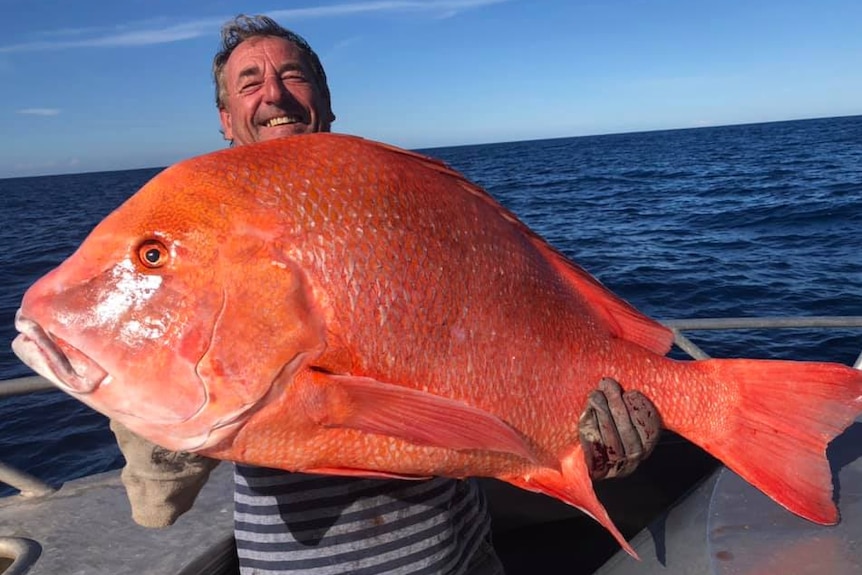 man holding large red coloured fish with ocean in the background