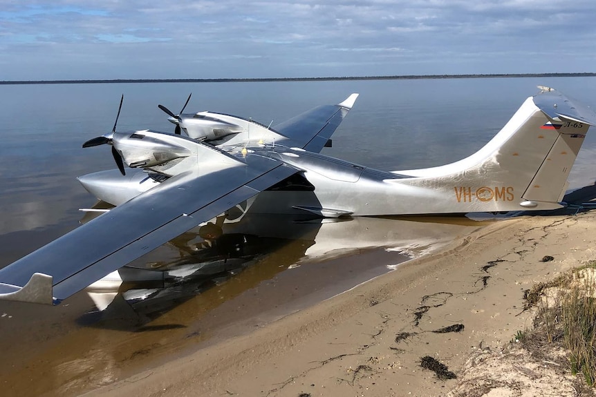 A silver seaplane parked in shallow water on a beach