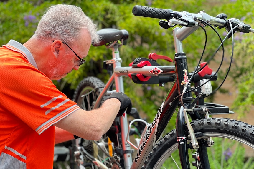 A man with grey hair and glasses works on a mountain bike