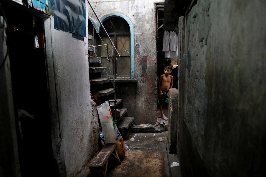 A little boy stands in a dark alleyway.