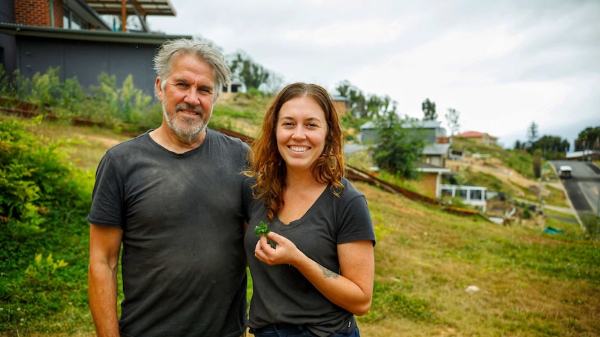 A man with grey hair and young woman holding a green plant stand on a block of land.