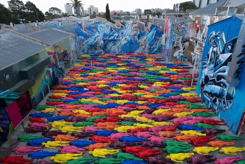 Multiple naked people in multi-coloured body paint.