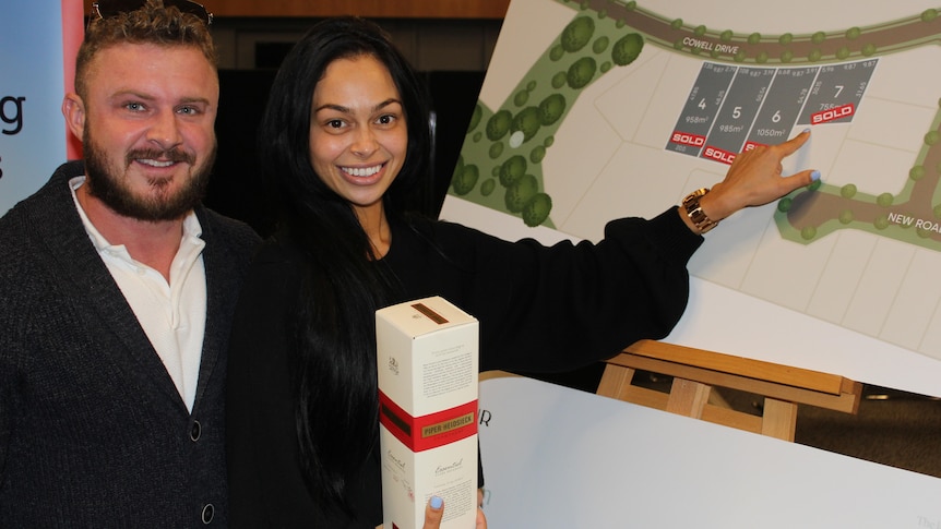 Couple holding champagne pointing to a poster with housing development layout