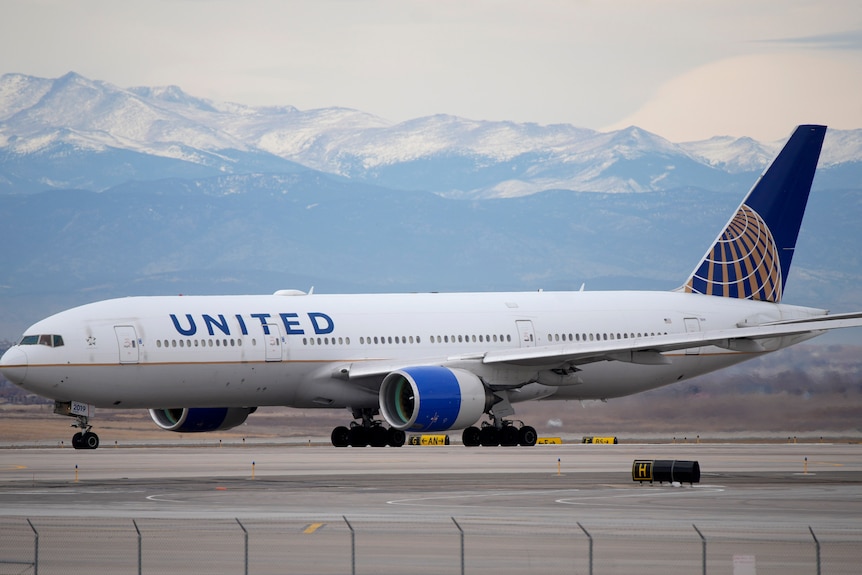 A United Airlines jetliner taxis to a runway with mountains in the background.