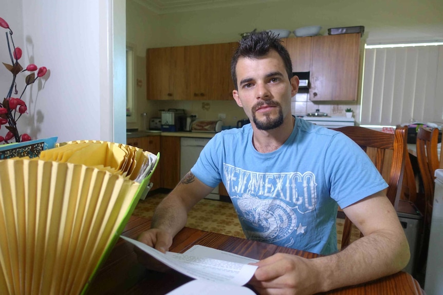 A young man holding paperwork in his kitchen.