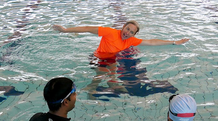 A woman, wearing an orange rashie, teaches swimming to adults