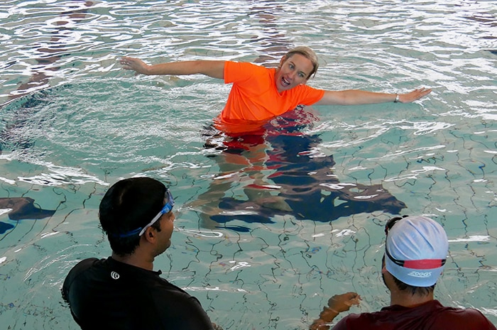 A woman, wearing an orange rashie, teaches swimming to adults