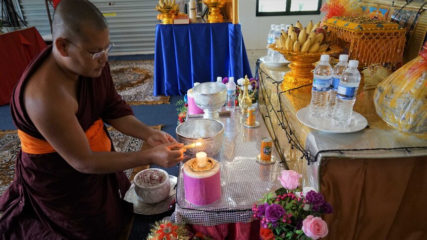 Monk lighting candle at temple in Humpty Doo, May 2020.