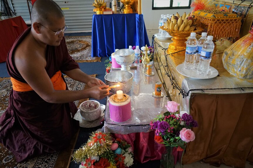 Monk lighting candle at temple in Humpty Doo, May 2020.