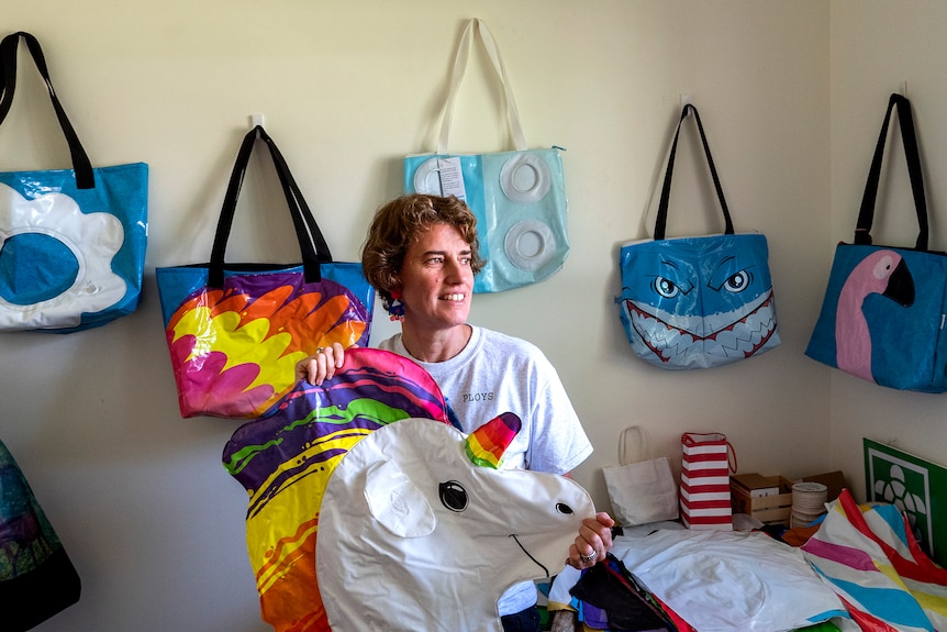 A woman holds an old pool toy unicorn with colourful bags made from PVC behind her.