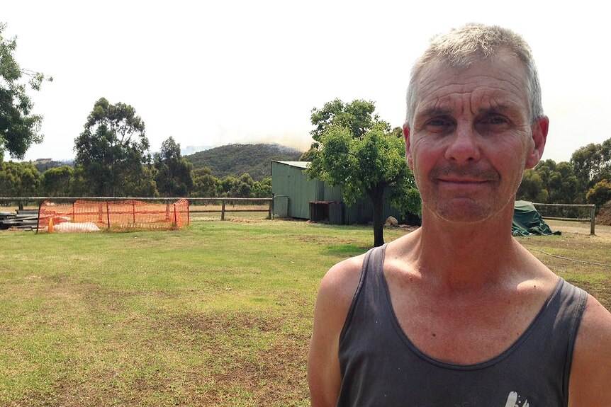 Yundi resident Rob Bowker stands on his property with a bushfire in the background.