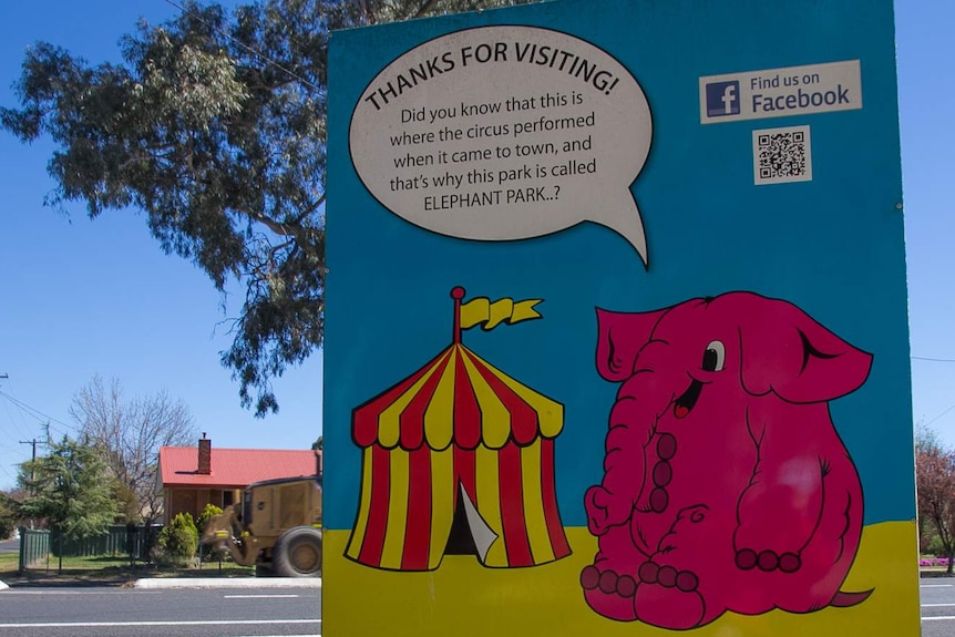 A sign with a picture of a pink cartoon elephant and a circus tent