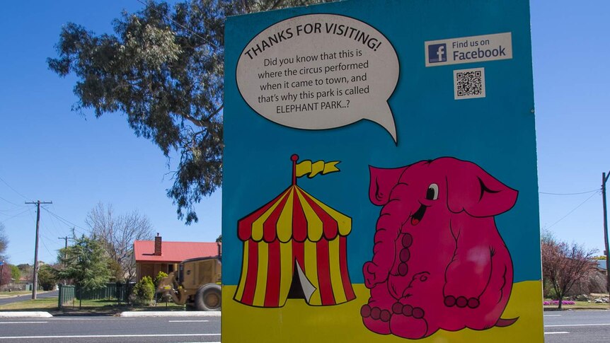 A sign with a picture of a pink cartoon elephant and a circus tent