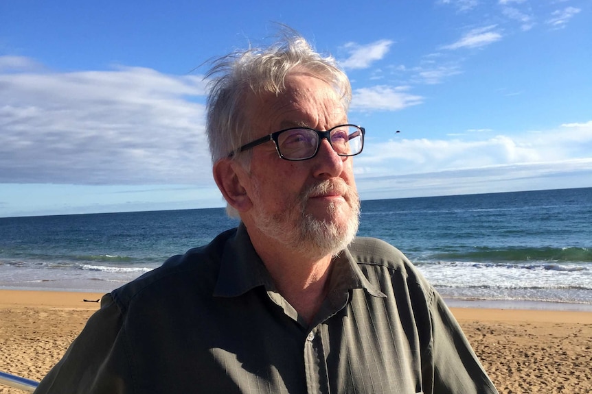 Headshot of a man with a beach in the background.