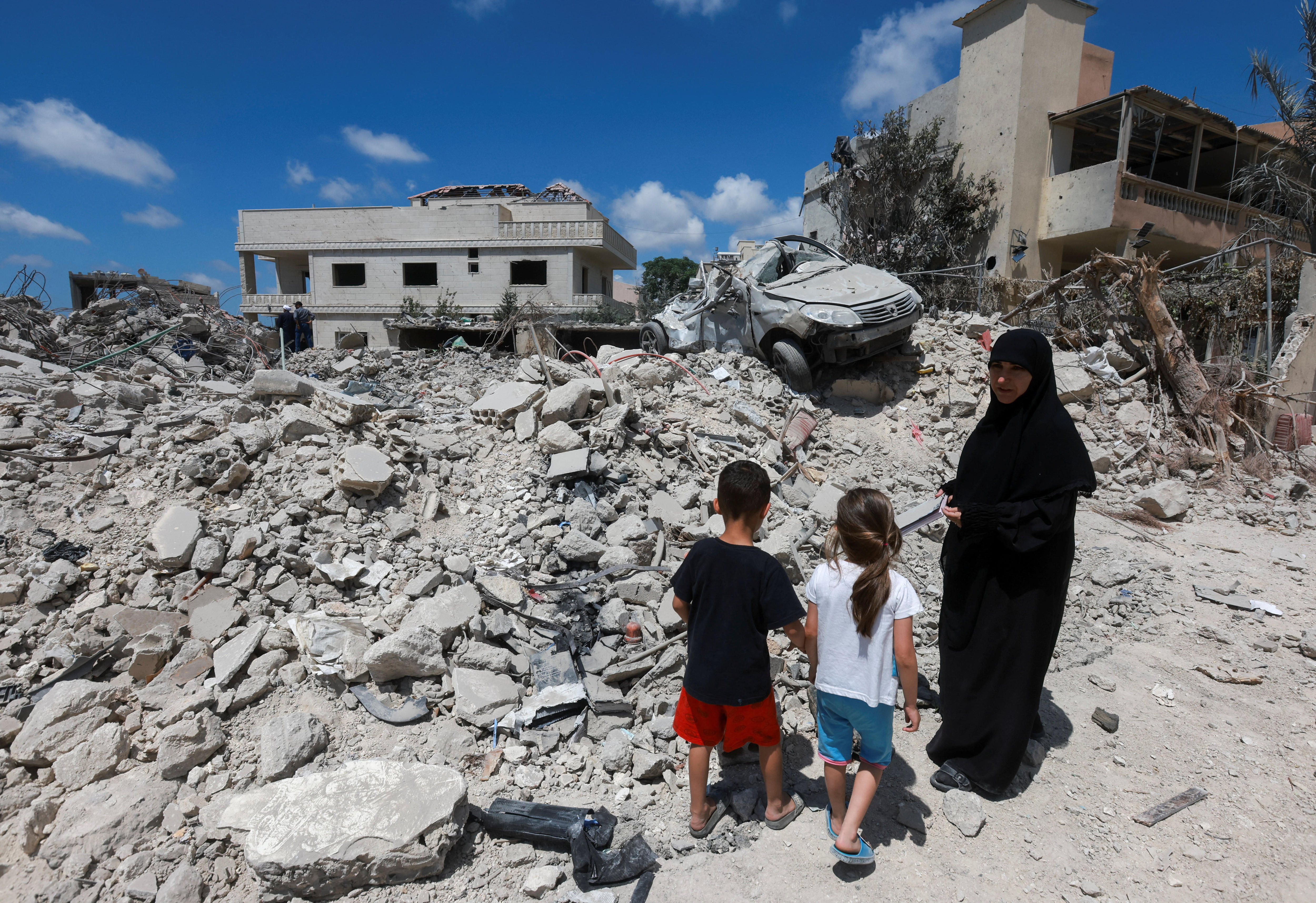 A woman stands with children next to piles of rubble from destroyed buildings in south lebanon.