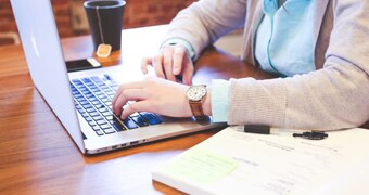 A woman on a laptop with an open book next to it