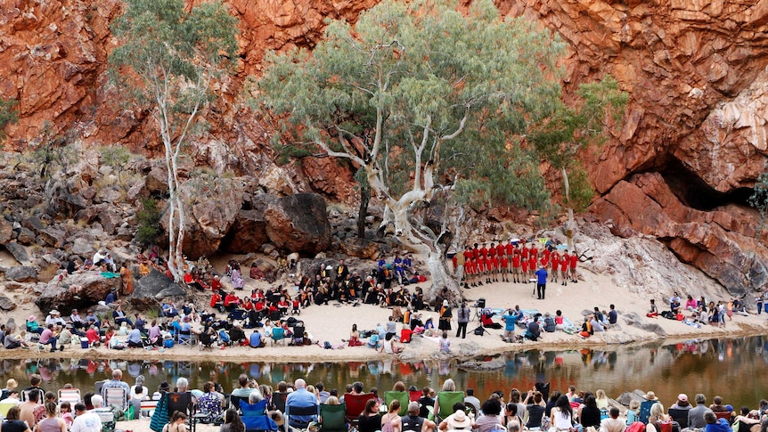 View of the choir singing in the distance with audience looking on, gorge in the backgrounf