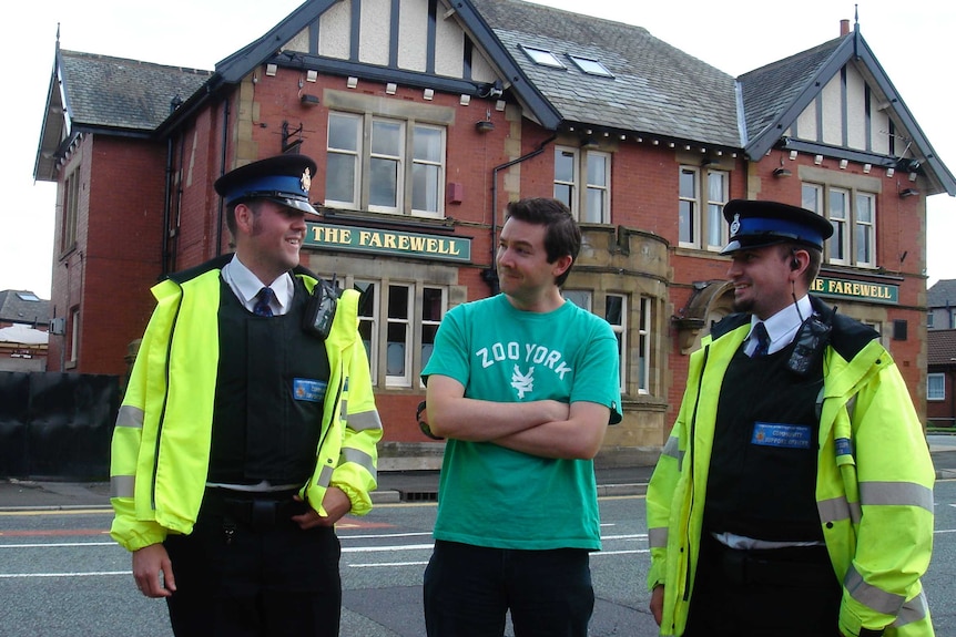 Michael Tetlow stands between two British police officers in front of the Farewell Inn pub.