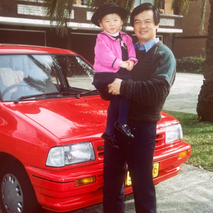 Emily Sun as a small child, wearing a black hat and held by her dad, Daniel.