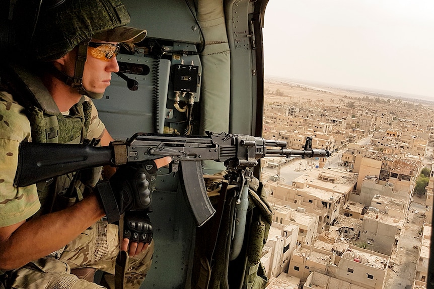 A Russian soldier holding a gun looks over Palmyra, Syria, from a military helicopter.