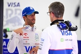 Daniel Ricciardo, in his racing suit, talking to a team member in their F1 garage.
