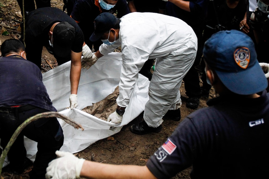 Malaysian police forensic team members bent over an unmarked grave.