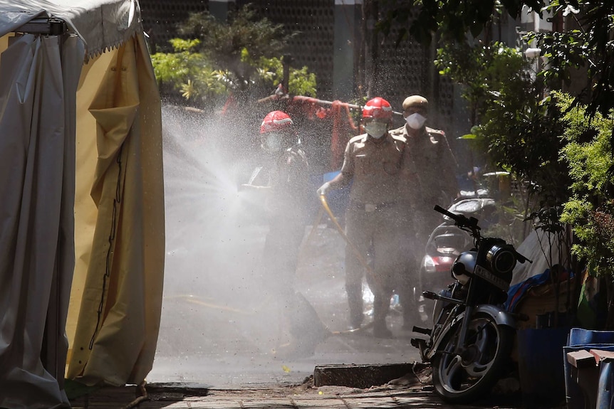 Three men in suits and masks hold hoses as they spray a tent.