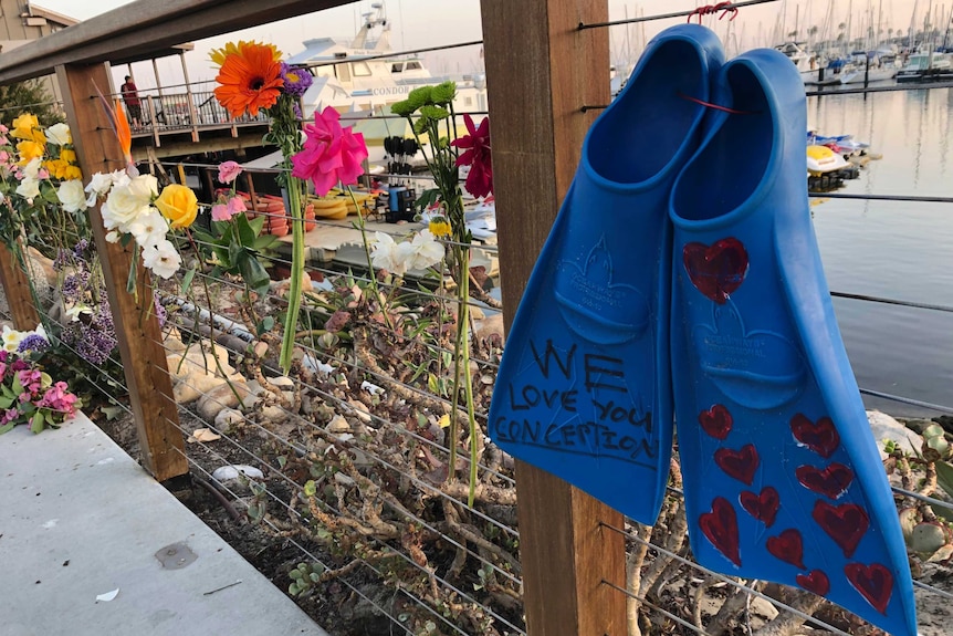A pair of blue flippers tied to a fence with "we love you Conception" written on them. Flowers are also hung on the fence.