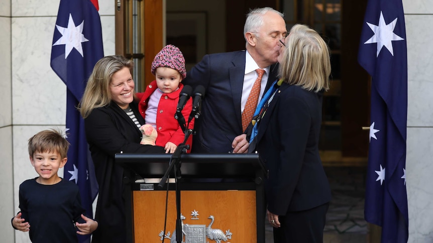 Malcolm Turnbull gives his wife a kiss on the lips as he stands with a youn woman holding a baby, and a young boy