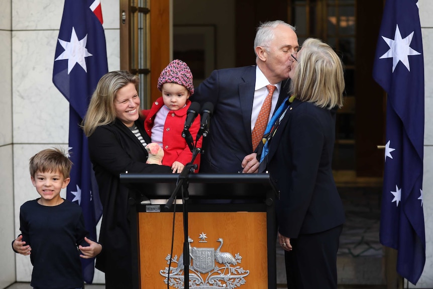 Malcolm Turnbull gives his wife a kiss on the lips as he stands with a youn woman holding a baby, and a young boy