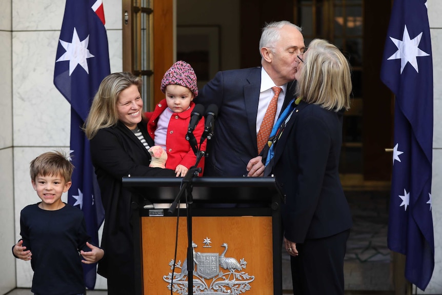 Malcolm Turnbull gives his wife a kiss on the lips as he stands with a young woman holding a baby, and a young boy