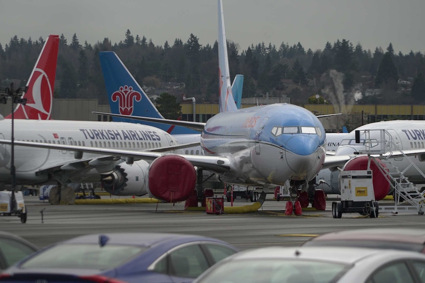 Three Boeing 737 MAX planes parked at the factory near a carpark.