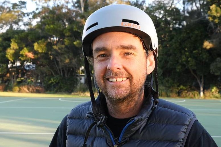 A man in his late 30s with a helmet on unclipped and puffy vest.