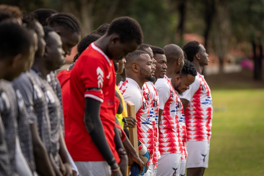 Soccer players line up with bowed heads for a guard of honour to remember their team mate