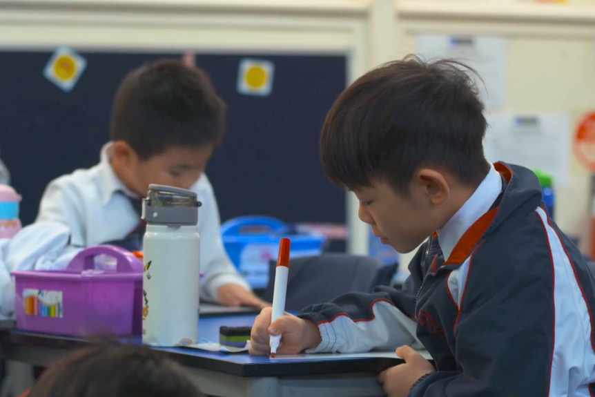 Two young boys of Asian background writing in a classroom