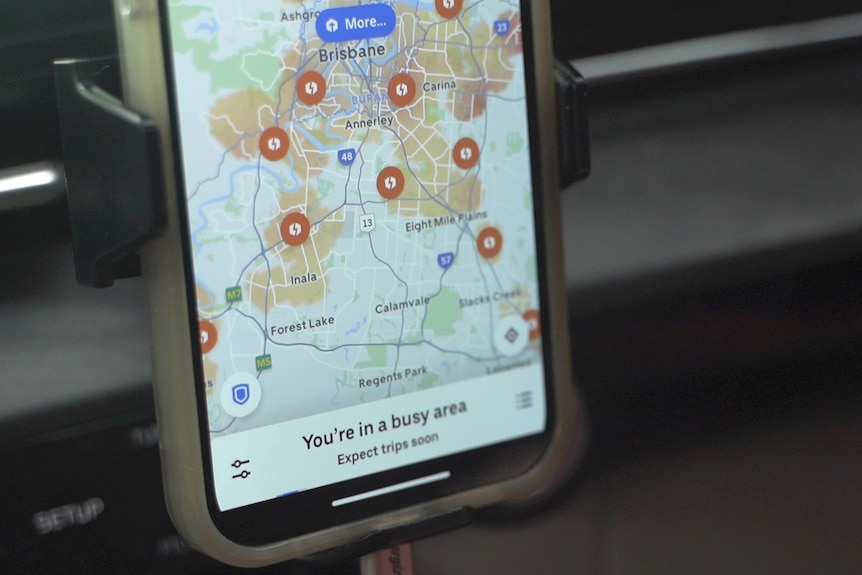 Uber app saying 'You're in a busy area' at bottom of phone screen and map of Brisbane above
