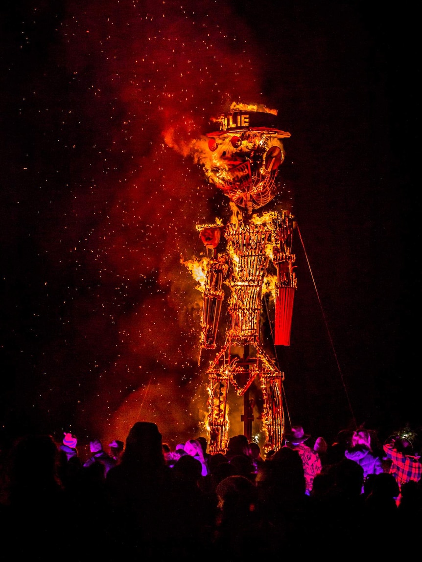 A large wicker man is set alight at night in front of a crowd of onlookers.