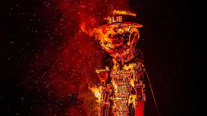 A large wicker man is set alight at night in front of a crowd of onlookers.