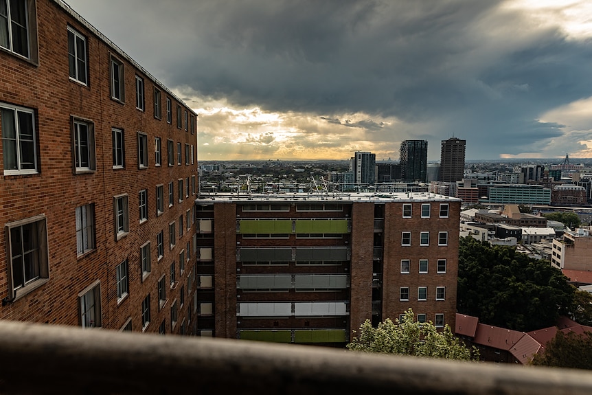 A tall housing estate with incomplete construction as the sun shines through storm clouds 