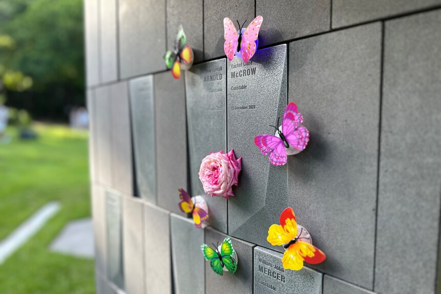 a close up image of a memorial wall with flowers and butterflies placed on the rock
