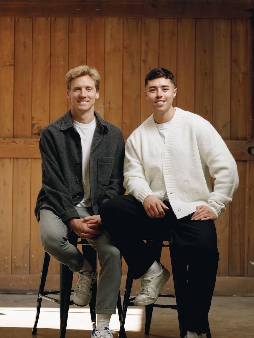 Brett wears a dark jacket and white shirt and Brad wears a white cardigan. Both are smiling at the camera.