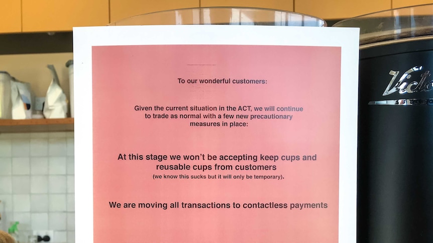 A sign in a cafe tells customers it cannot accept cash or keep cups.