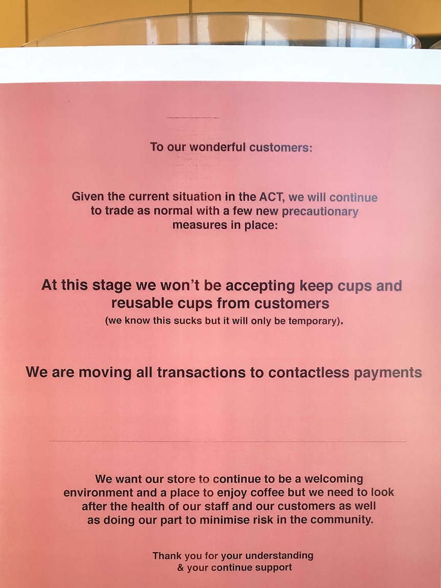 A sign in a cafe tells customers it cannot accept cash or keep cups.