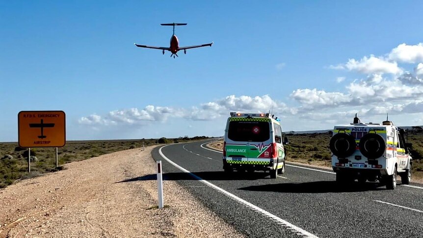 Ambulances wait as a plane lands on the road.